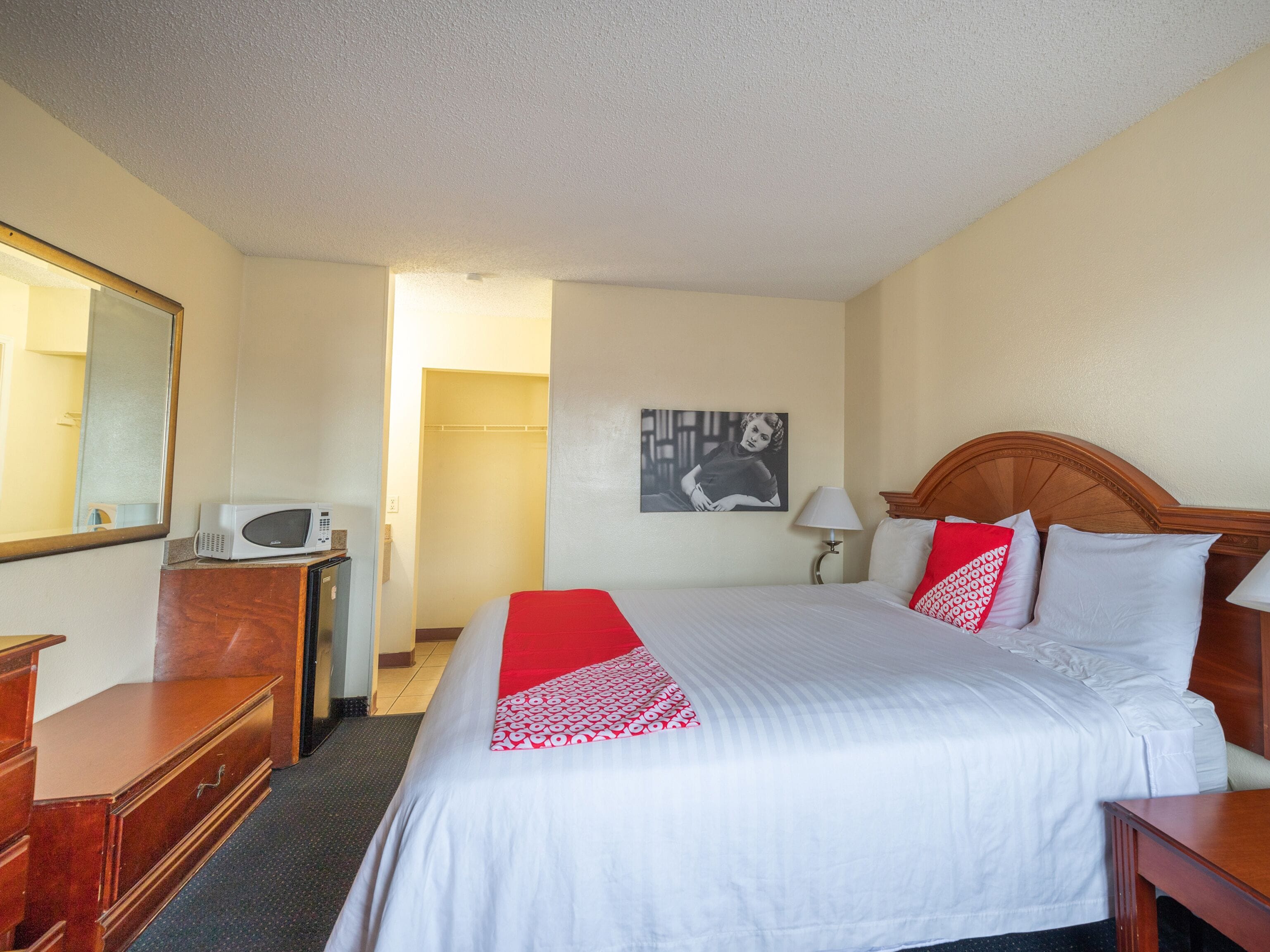 A hotel room with a large bed, a wooden dresser, a microwave, a mirror, and a door leading to another room.
