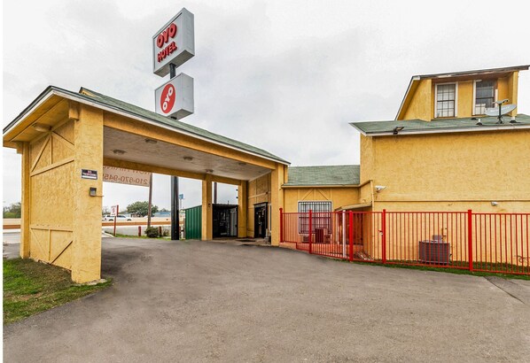 A hotel with a covered entrance, a red fence, and a satellite dish on the roof.