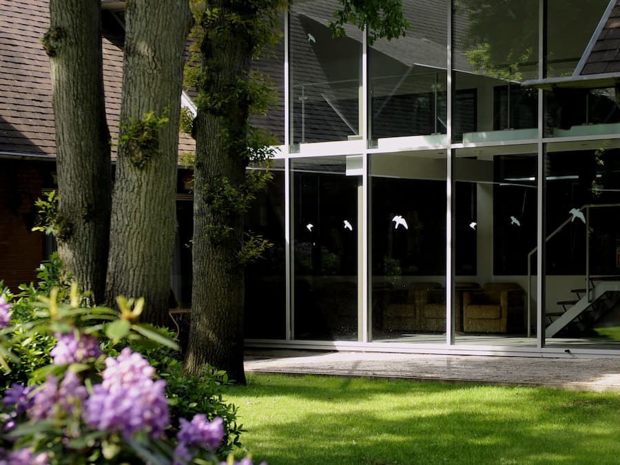 A modern building with large glass windows, a grassy lawn, and trees.
