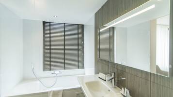 A modern bathroom with a bathtub, a large mirror, and a window with blinds.
