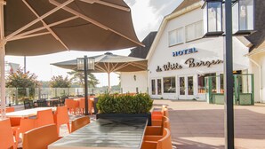 An outdoor seating area with tables and chairs, a building labeled "HOTEL de Witte Bergen," and a street lamp. - Van der Valk Hotel Hilversum - de Witte Bergen (Eemnes)