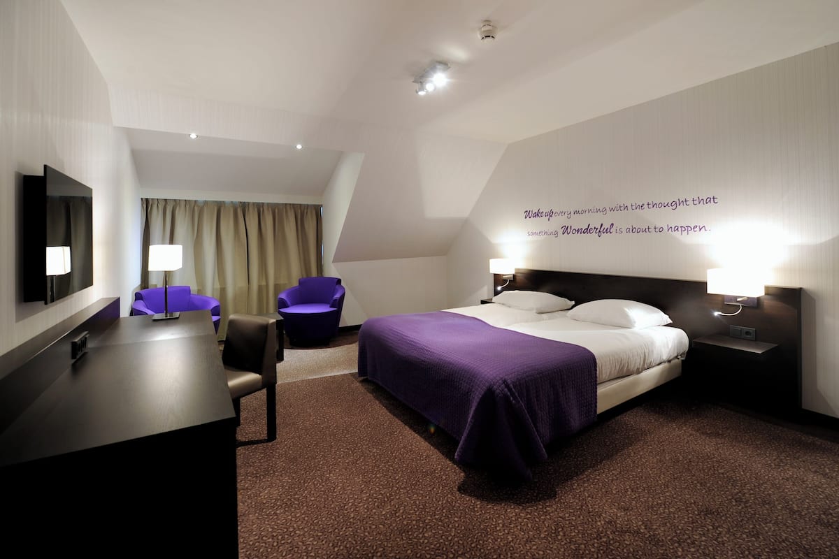 A hotel room with a bed, a desk, a chair, and a wall with a motivational quote.