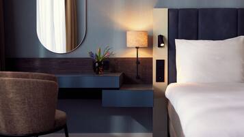 Una habitación de hotel moderna con una cama, un escritorio con lámpara, una silla y un espejo.