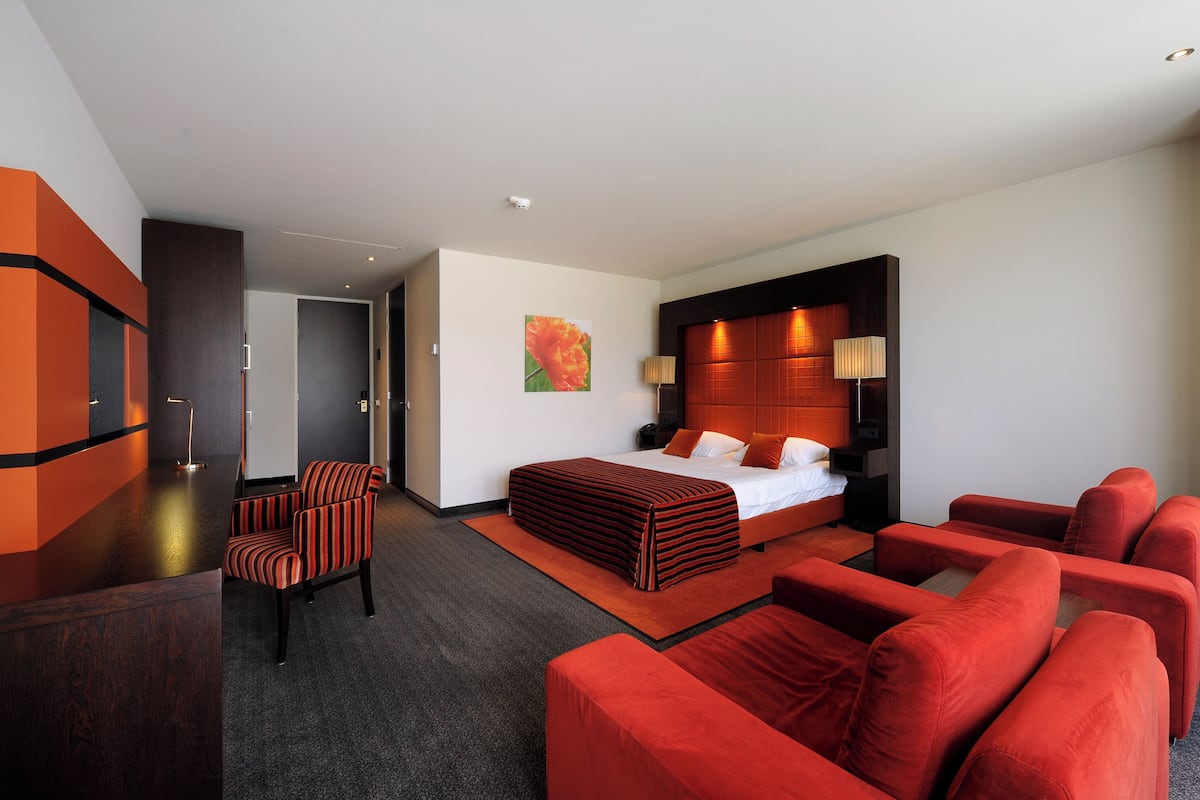 A hotel room with a large bed, a sitting area with red sofas, a desk, and a chair.