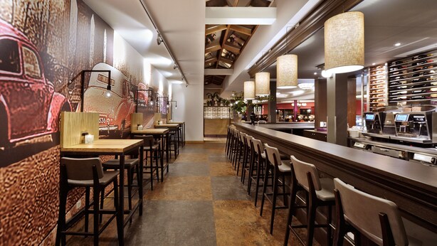 A modern restaurant with high ceilings, exposed beams, and a long bar area with stools. - Van der Valk Hotel Hilversum - de Witte Bergen (Eemnes)