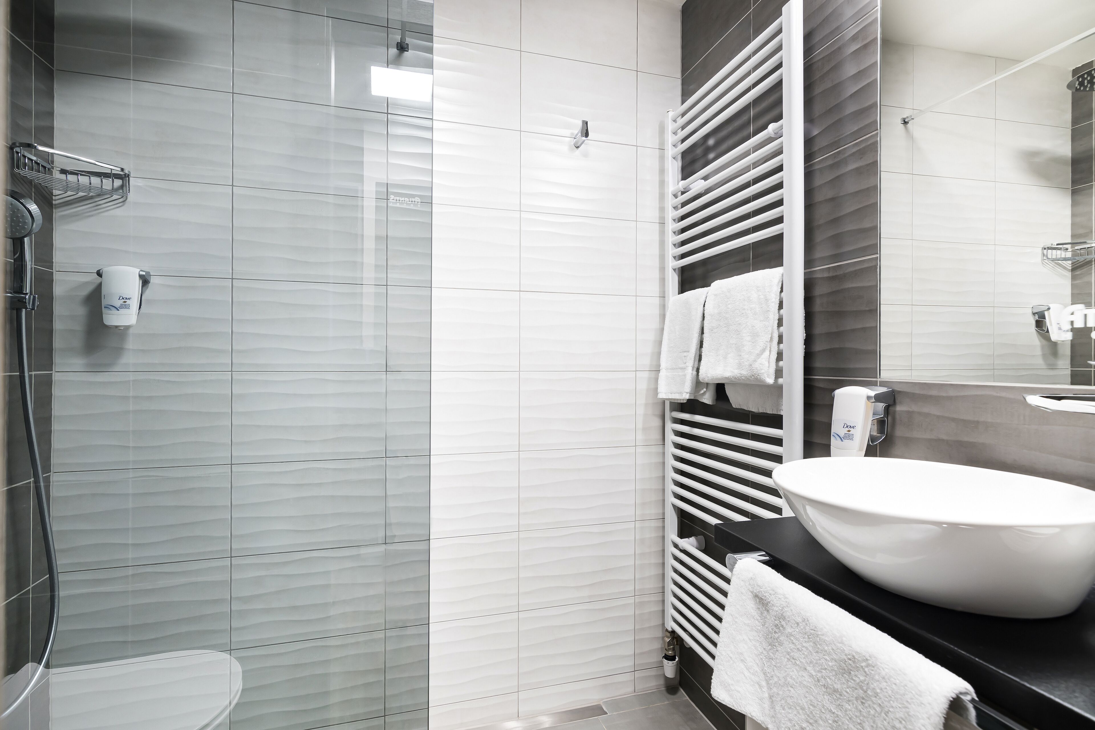 Un baño moderno con ducha acristalada, lavamanos blanco y un perchero para toallas.