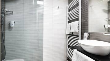 Un baño moderno con ducha acristalada, lavamanos blanco y un perchero para toallas.
