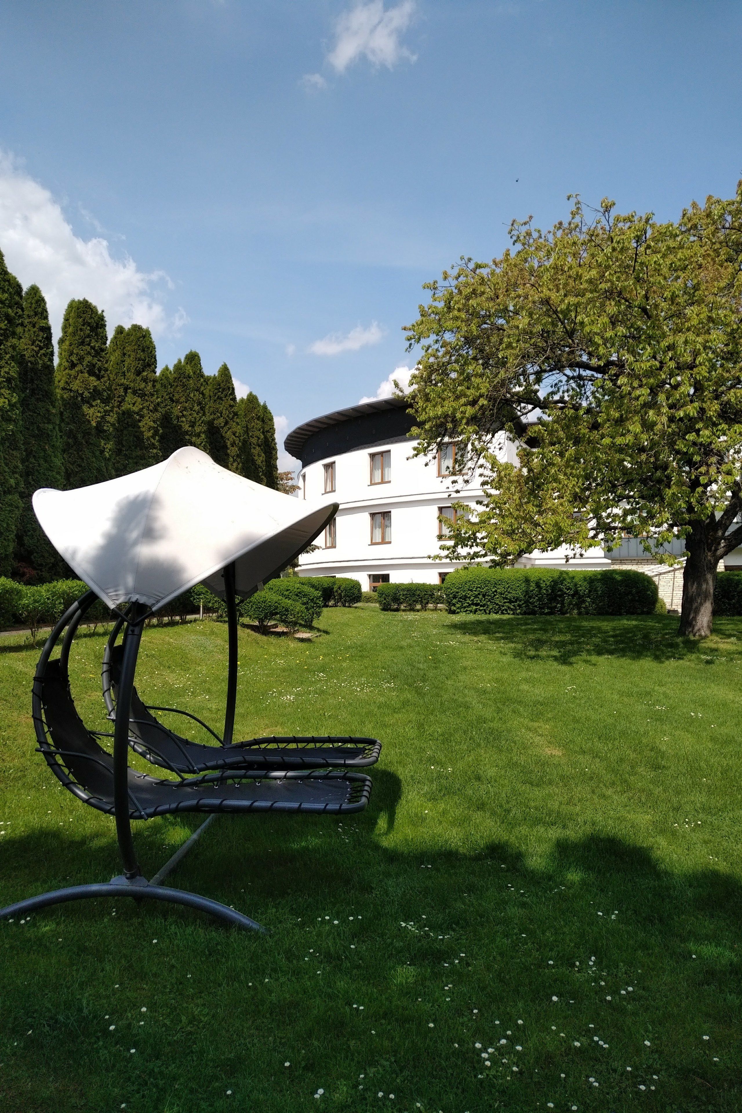 Un área de estar al aire libre de diseño moderno con una silla de diseño único, un césped cuidado y un edificio grande al fondo.