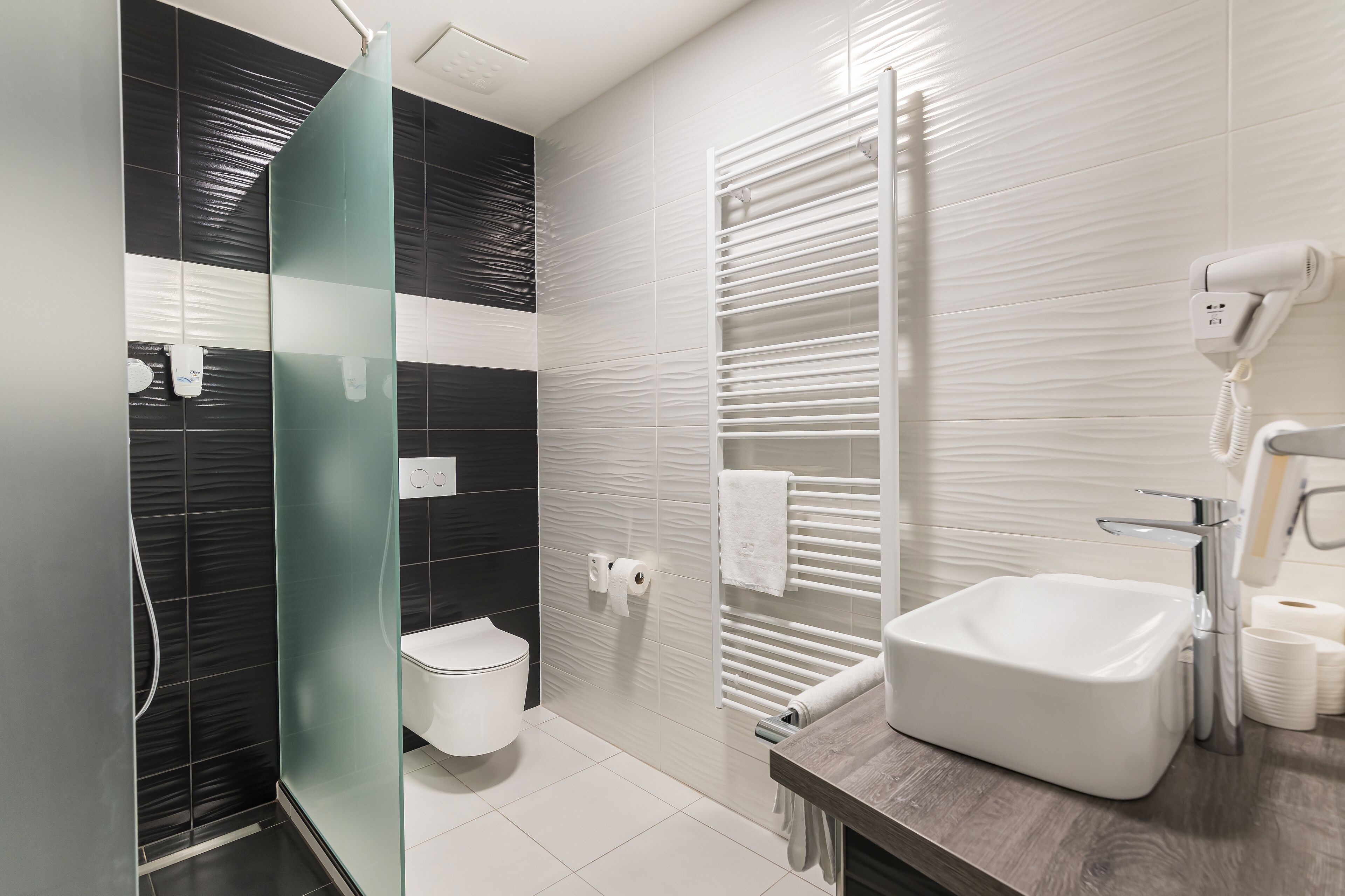 A modern bathroom with a glass shower enclosure, a white sink, and a towel rack.