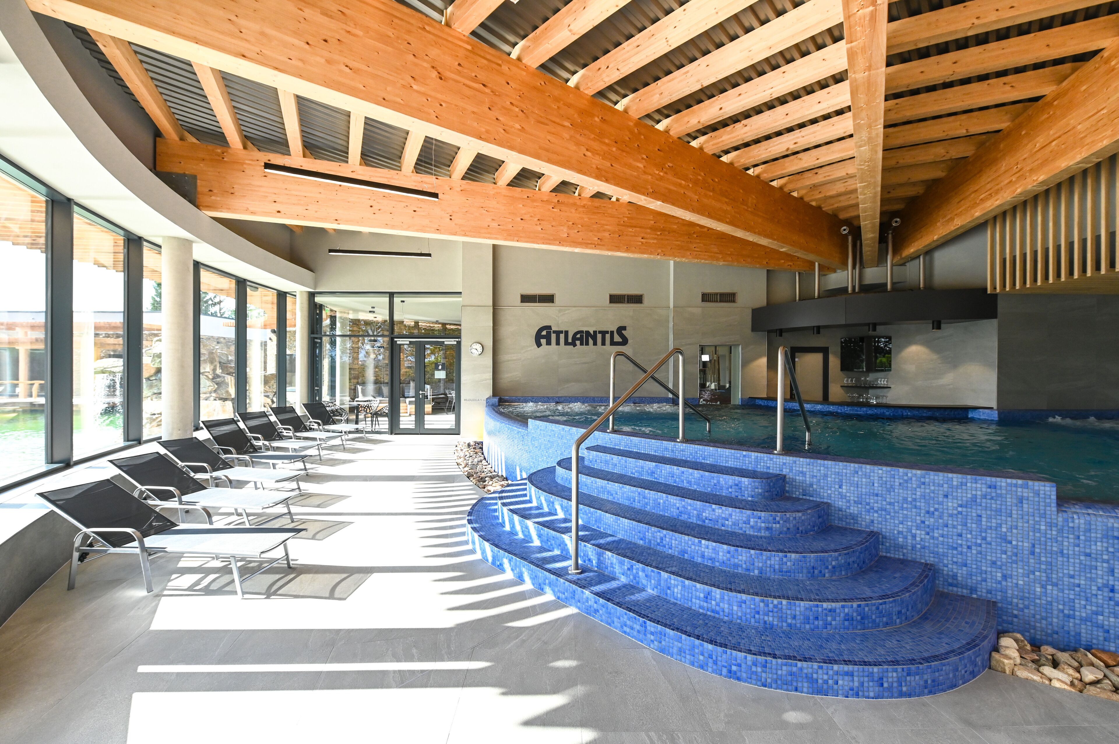 Zona de piscina con escalera de azulejos azules, sillas de descanso y techo de madera.
