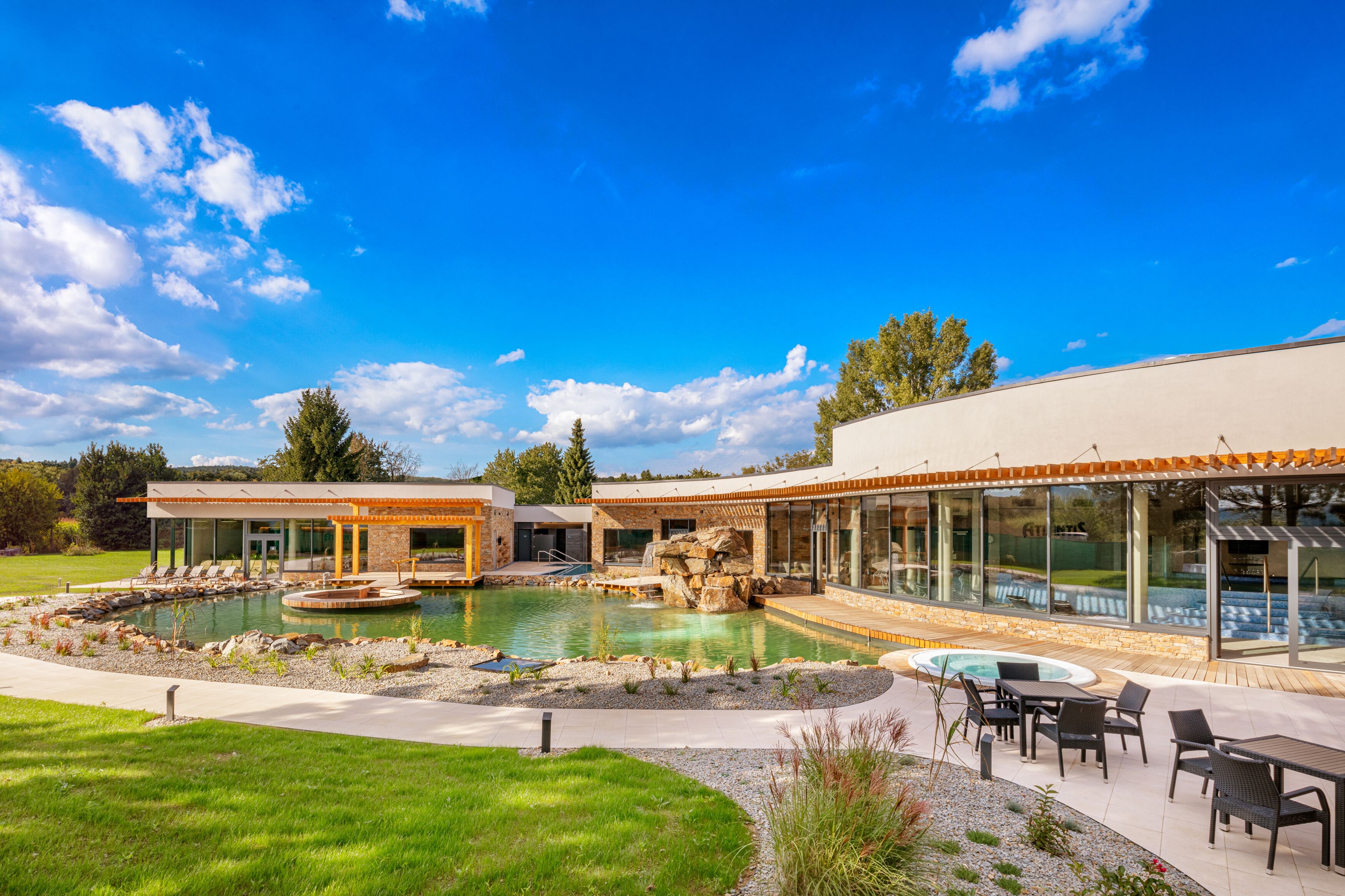 A modern resort with a swimming pool, outdoor seating, and a glass-enclosed spa area.