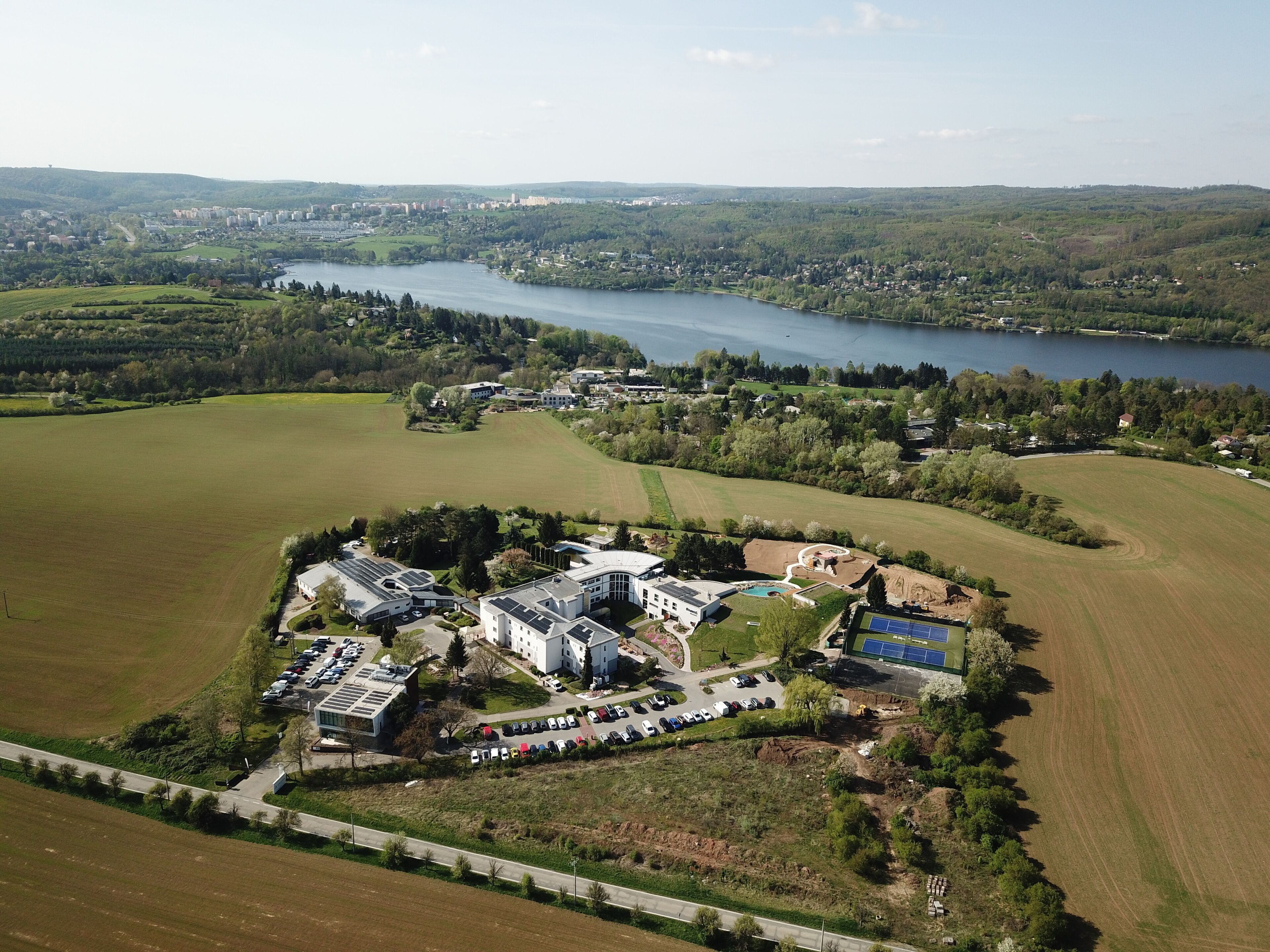 Vue aérienne d’un quartier résidentiel avec un grand plan d’eau, des champs verdoyants et un ensemble de bâtiments modernes dotés de panneaux solaires.
