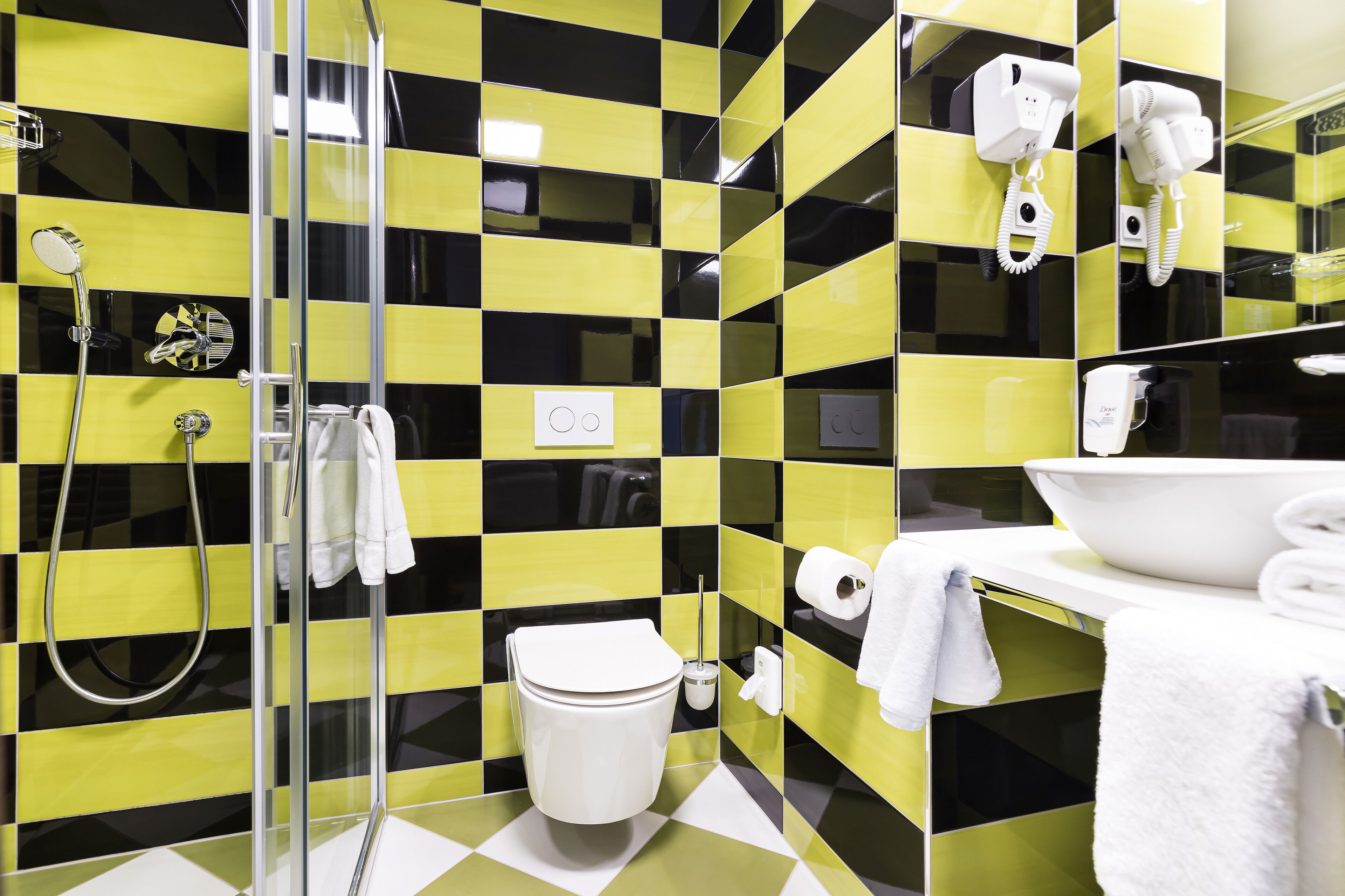 A bathroom with a checkered yellow and black tile pattern, a glass shower enclosure, a white toilet, a sink with a mirror, and a towel rack.