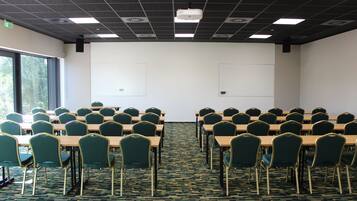 Una sala conferenze con file di tavoli e sedie, un proiettore e una lavagna.