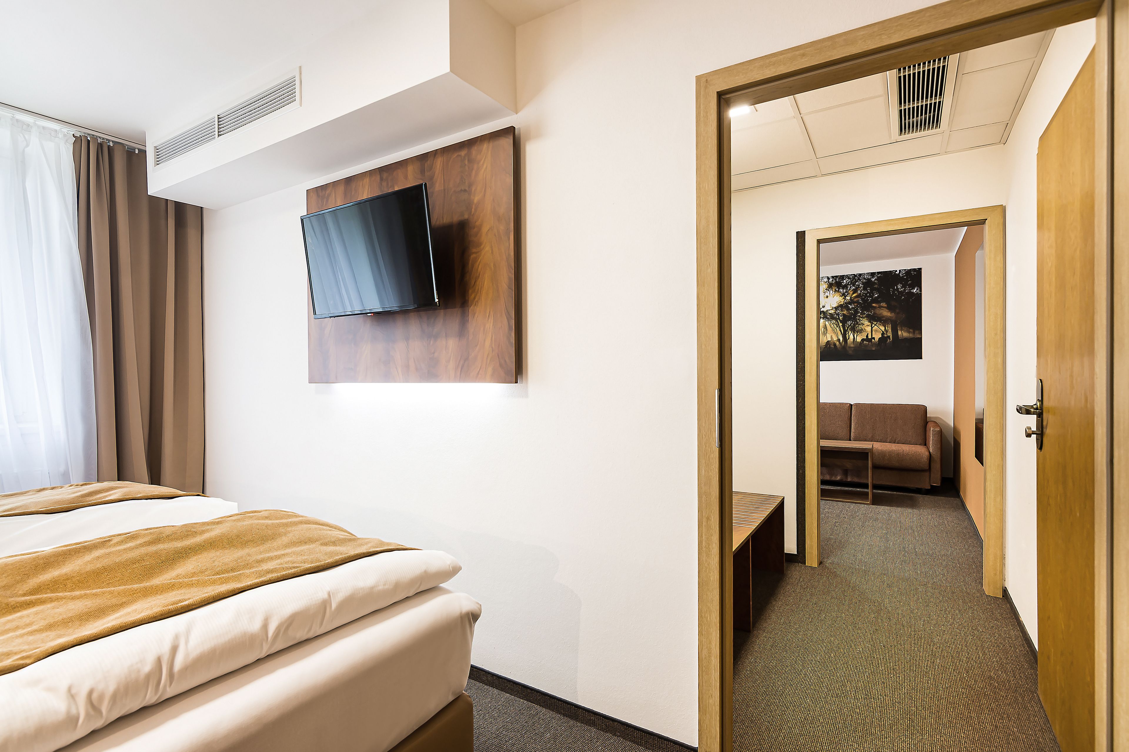 Een hotelkamer met een bed, een aan de muur bevestigde televisie, een deur naar een gang en een klein tafeltje.