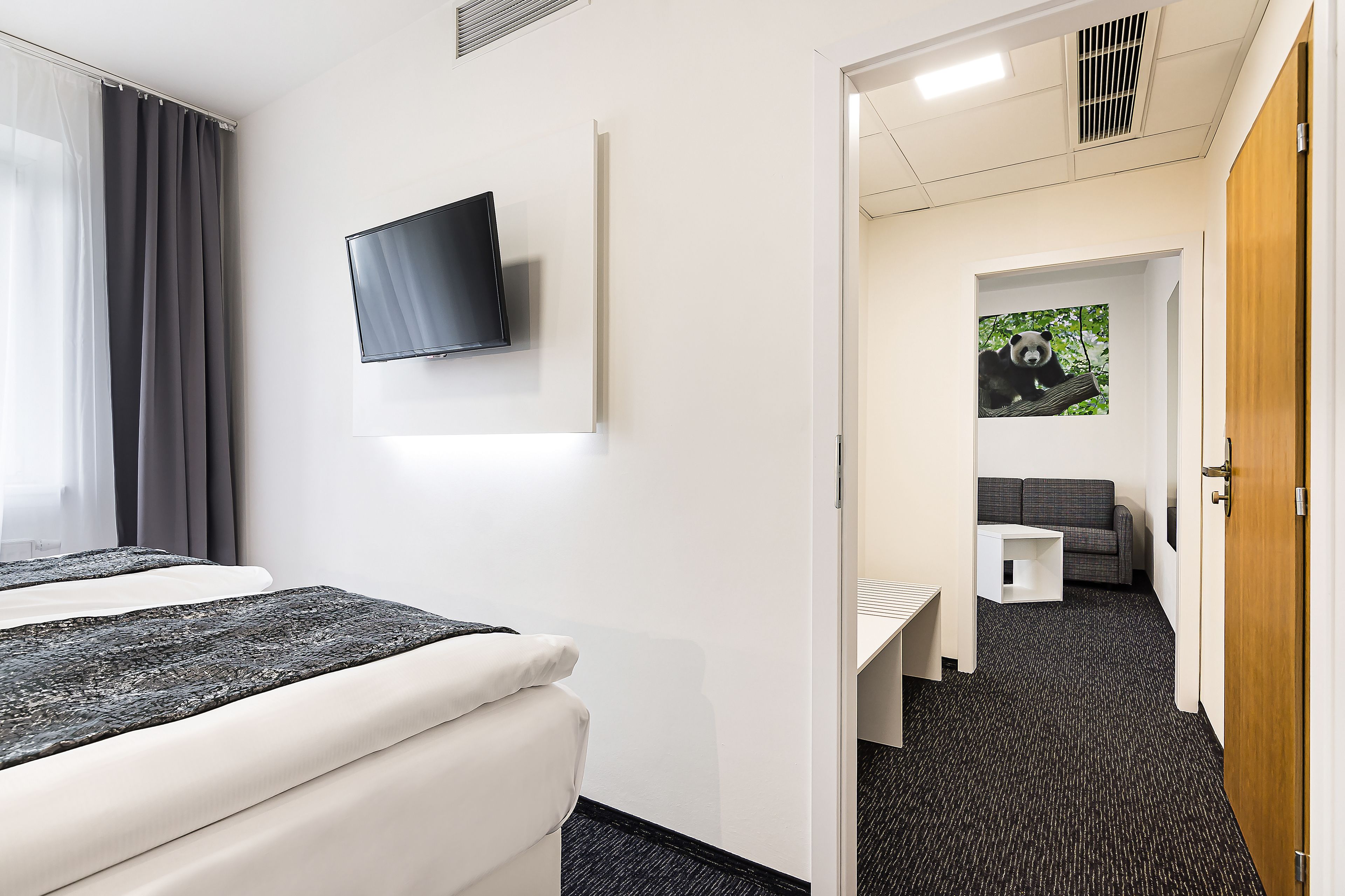 A hotel room with a bed, a TV, a small table, and a sofa.