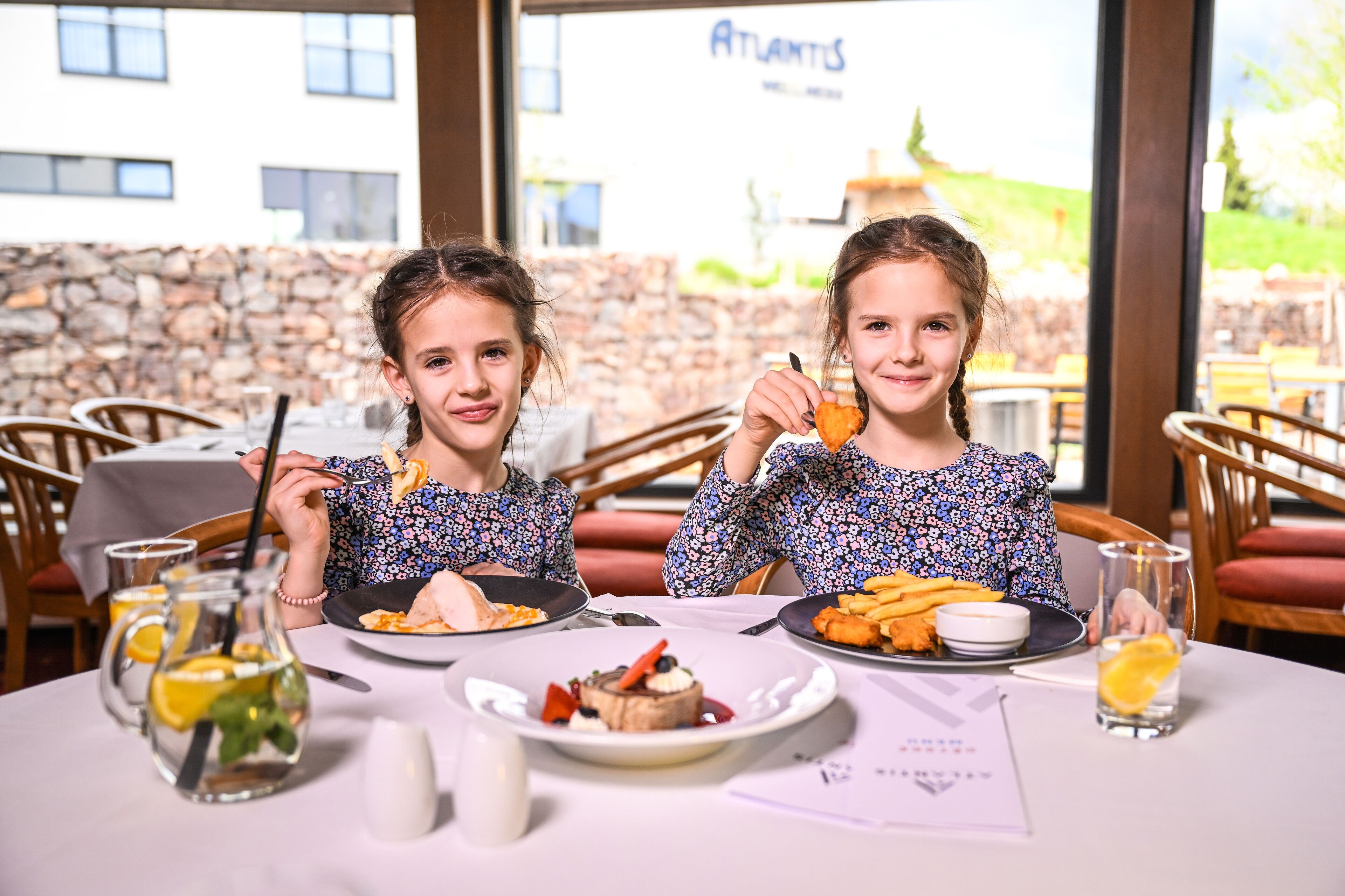 Twee personen dineren aan een tafel met borden eten, een limonadekan en een menukaart.