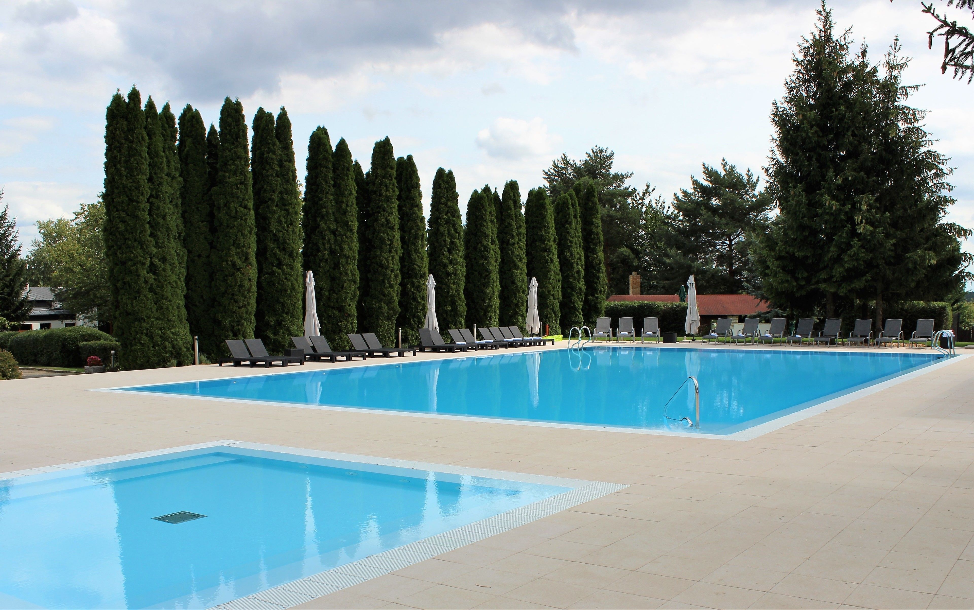 Una piscina con sillas de descanso y sombrillas, rodeada de altos árboles.