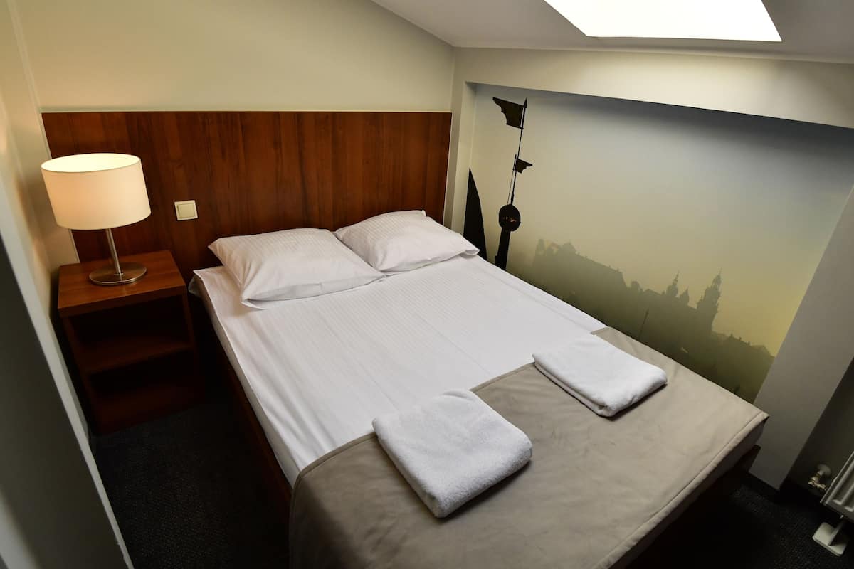 Quarto de hotel com cama, mesa de cabeceira, luminária e um mural na parede.
