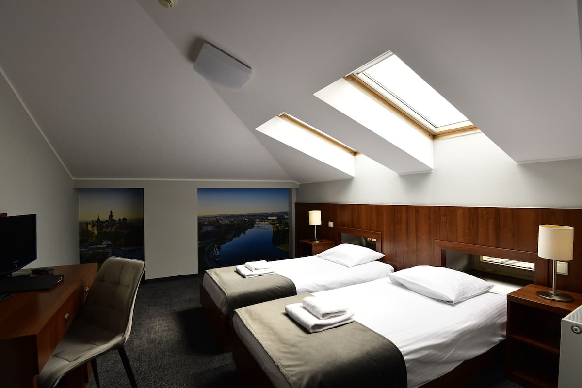Quarto de hotel com duas camas, uma escrivaninha, uma cadeira e claraboias.