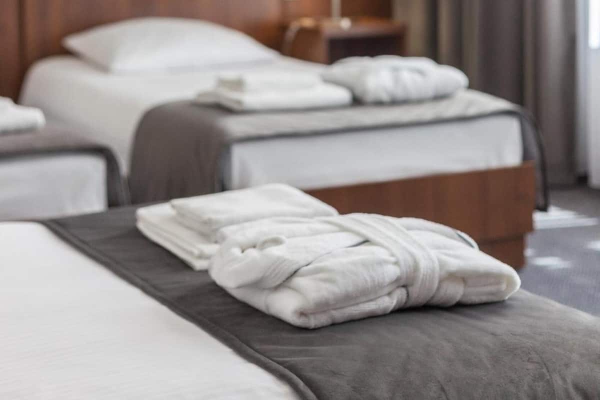 Quarto de hotel com uma cama grande, uma cama menor e uma mesa de cabeceira com abajur.