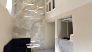 Un hall d’entrée moderne avec un mur en marbre, un canapé bleu foncé, une petite table ronde et un comptoir d’accueil doté d’un miroir.