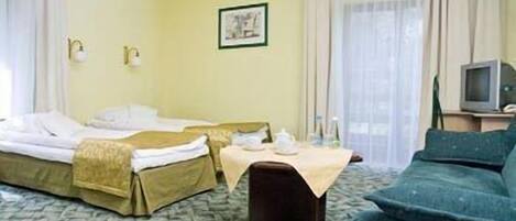 A hotel room with two beds, a small table with a teapot and cups, a television, and a couch.
