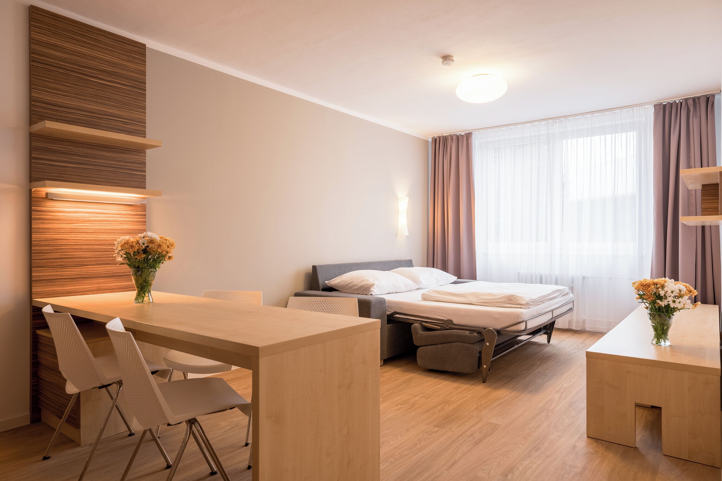 Una habitación de hotel moderna con un escritorio de madera, una cama y una pequeña zona de estar.