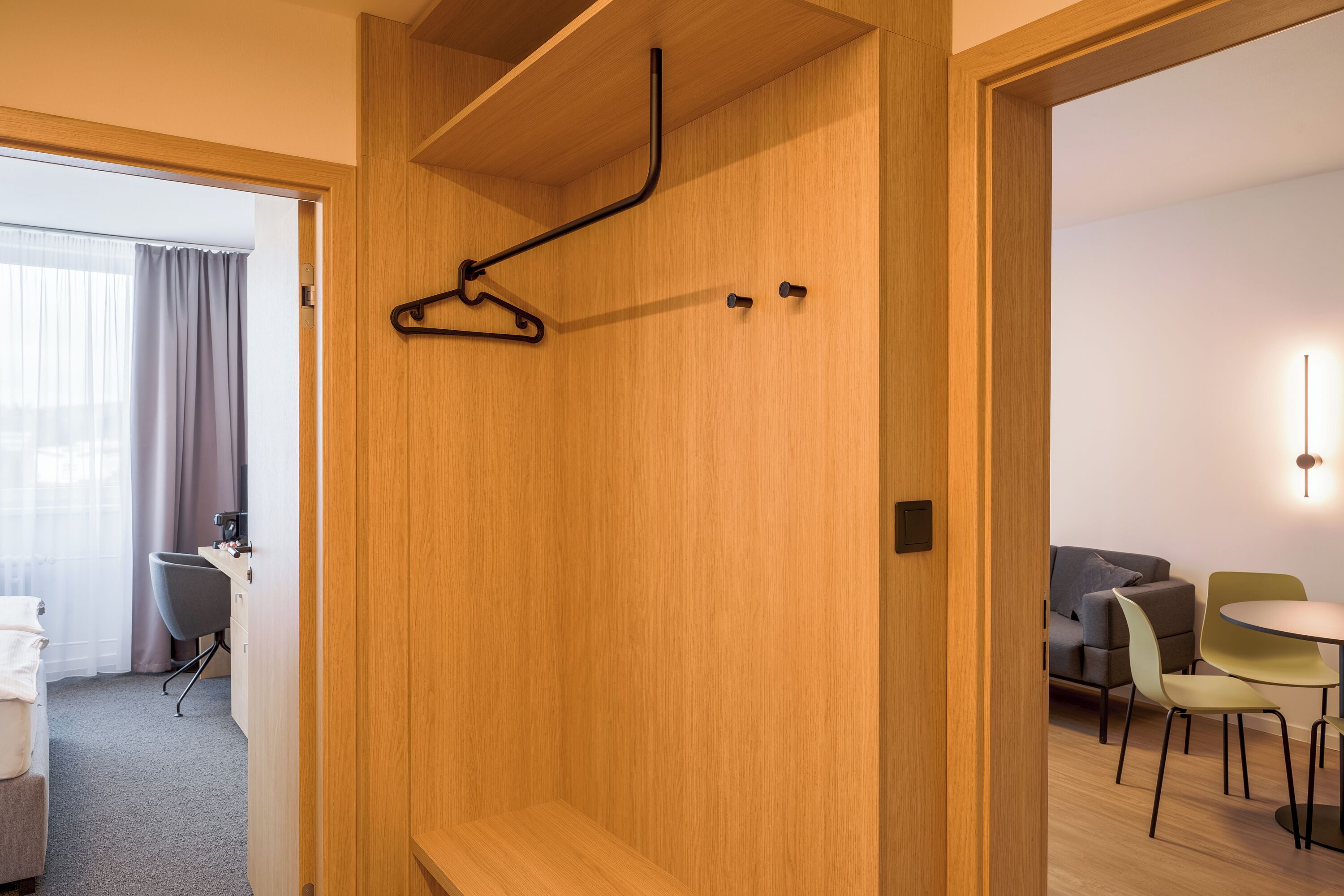 A hotel room with a wooden wardrobe, a hanging rack, a bed, a desk, and a seating area with chairs and a table.