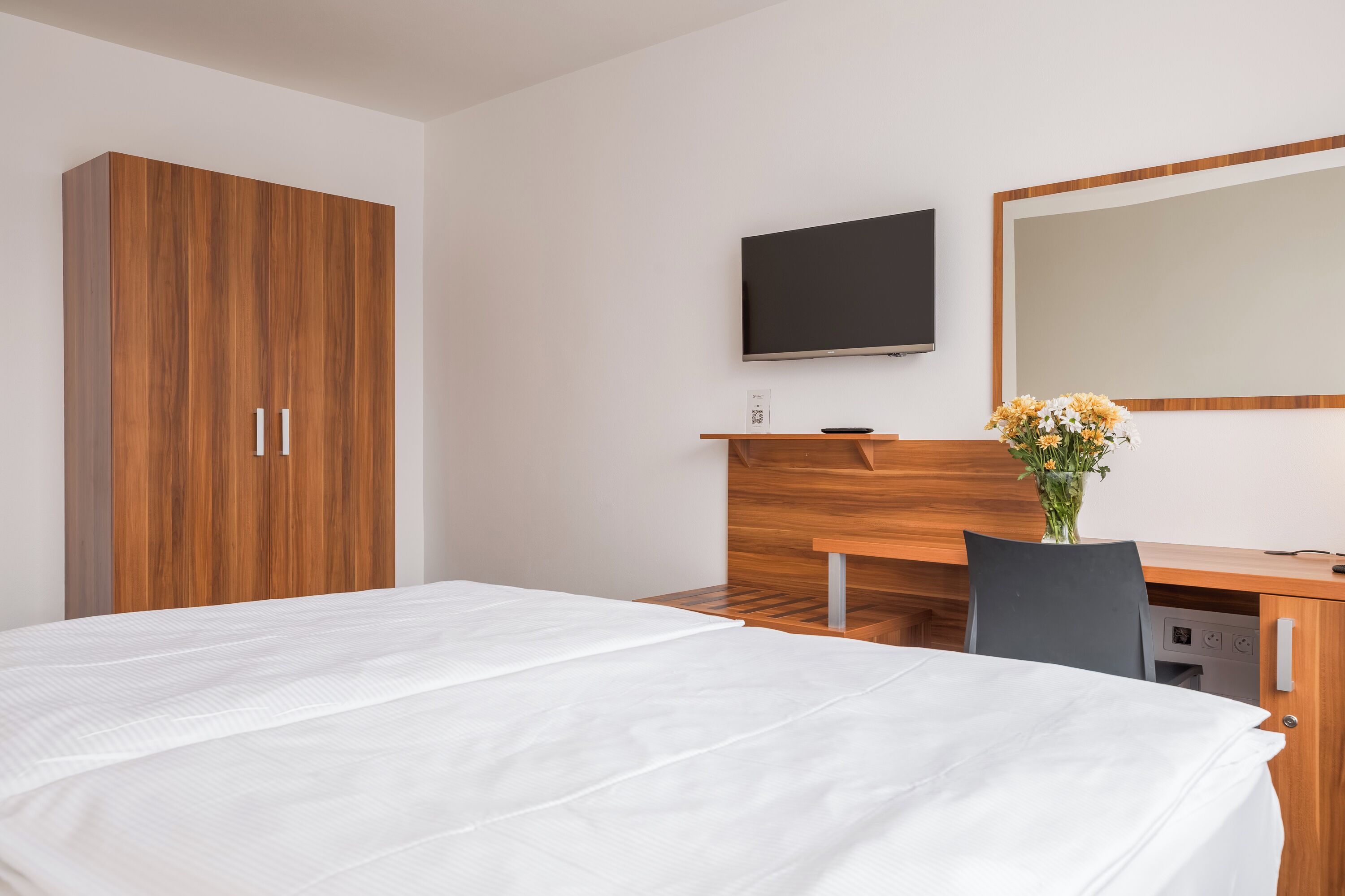 Une chambre d’hôtel avec un lit, un bureau en bois, une télévision et un miroir.