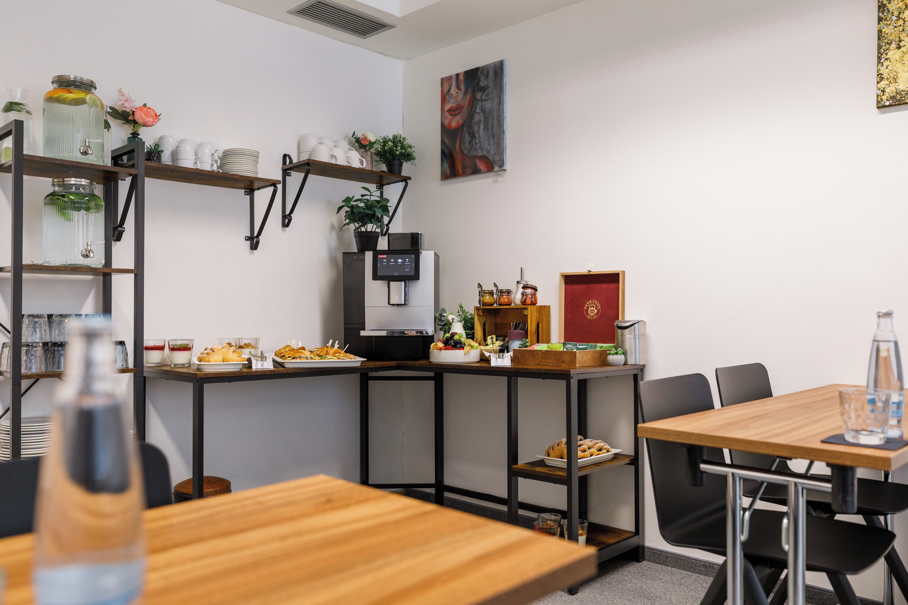 Eine moderne Küche mit Kaffeemaschine, Regalen voller Gläser und einem Essbereich mit Stühlen und Tisch.
