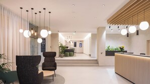Un área de recepción moderna con mostrador, zona de estar y una escalera que lleva a un nivel superior.