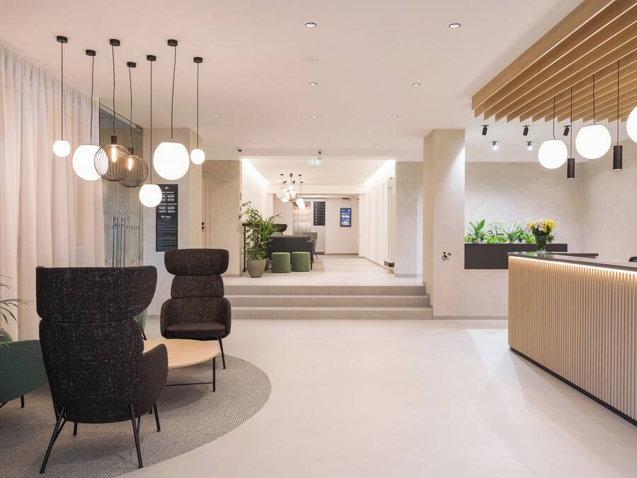 Un área de recepción moderna con mostrador, zona de estar y una escalera que lleva a un nivel superior.