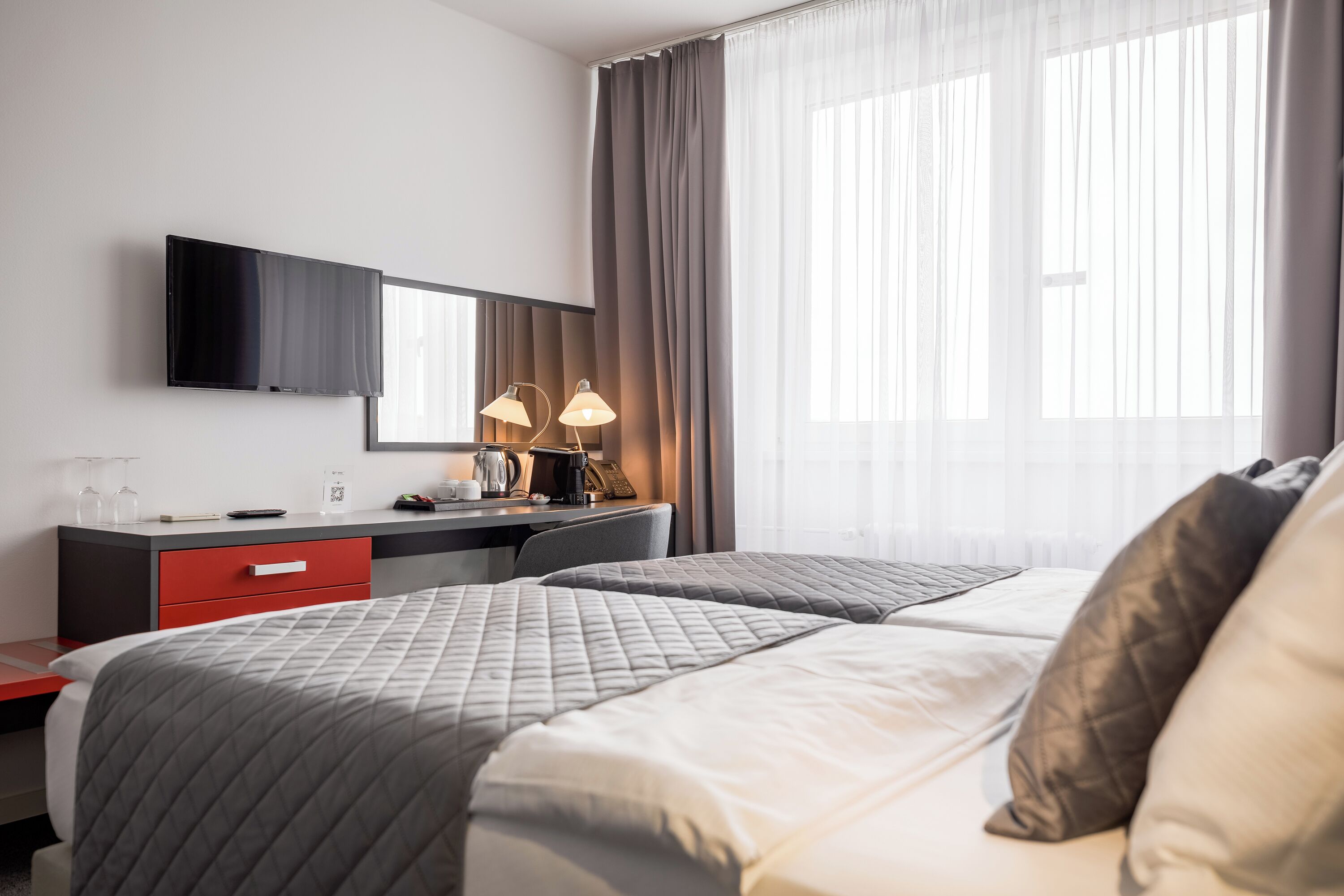 A hotel room with two beds, a desk with a flat-screen TV, a coffee maker, and a lamp.