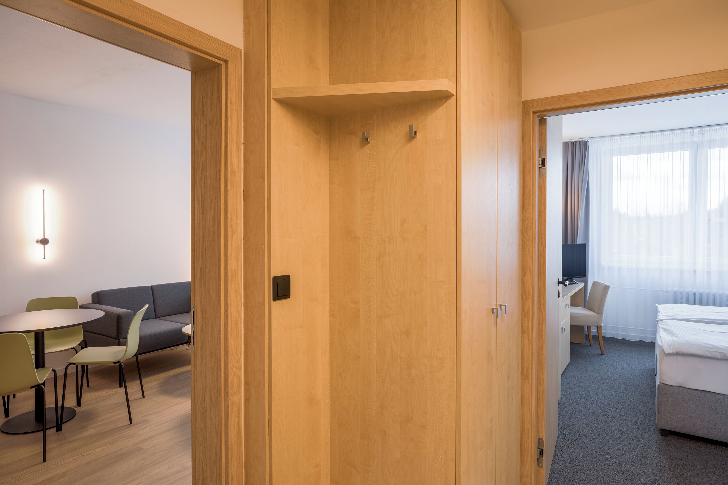 Una habitación de hotel con puerta de madera, un escritorio con silla, una cama y una pequeña mesa con sillas.