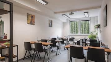 Een moderne vergaderzaal met meerdere tafels en stoelen, grote ramen met uitzicht op bomen en kunstwerken aan de muren.
