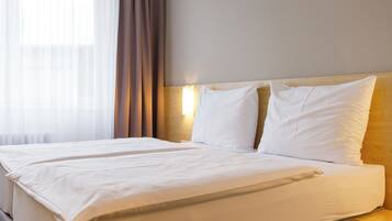 A double bed with white linens, a wooden headboard, and a bedside table with a lamp.