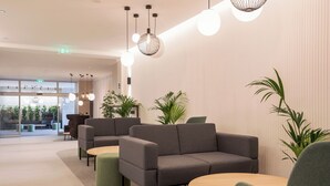 Un vestíbulo moderno con un sofá gris, mesas redondas, lámparas colgantes y plantas en macetas.