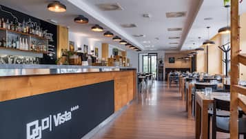 A modern restaurant interior with a bar area, wooden tables, and pendant lighting.