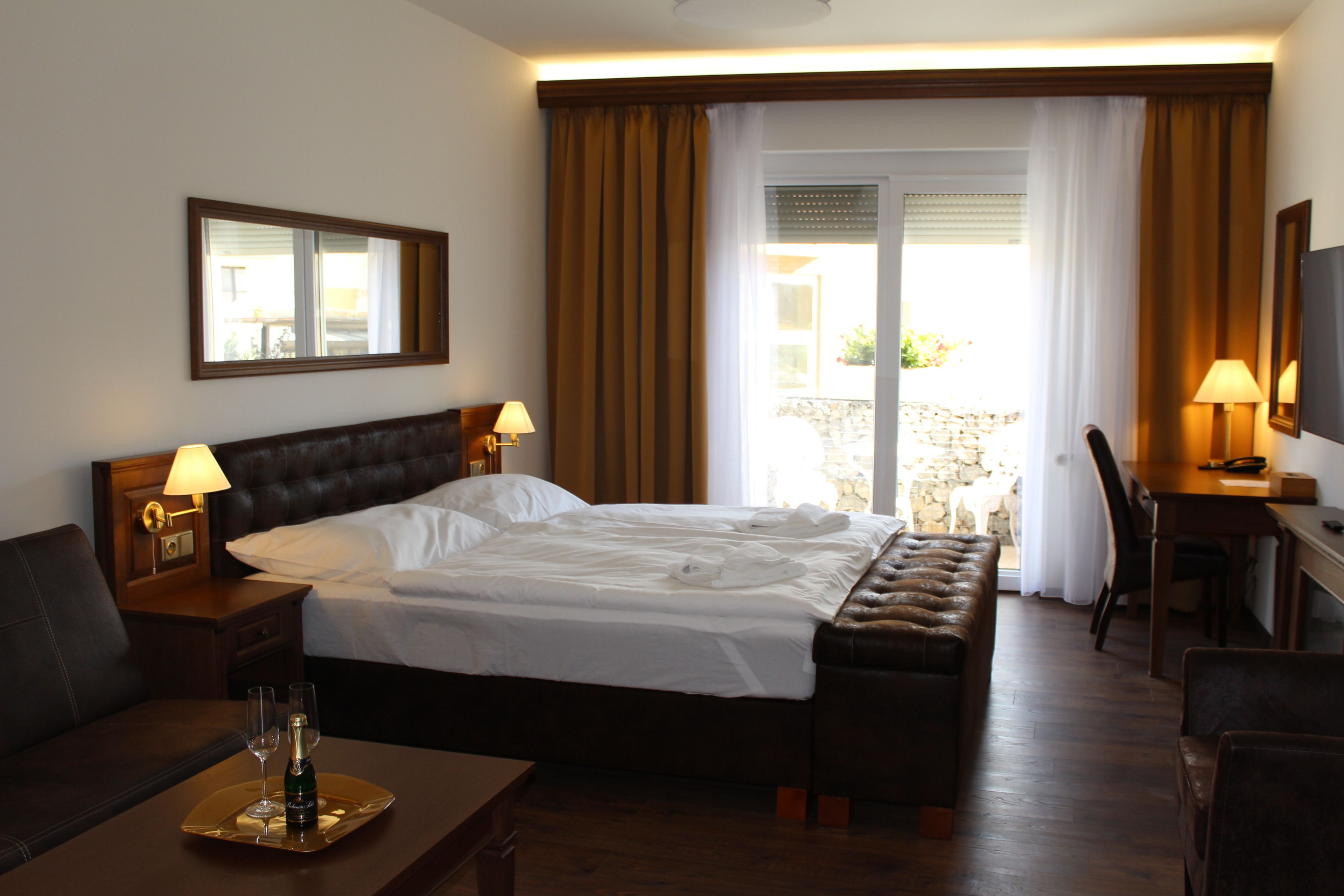 Ein Hotelzimmer mit einem großen Bett, einem Schreibtisch, einem Sessel, einem Fernseher und einem Balkon mit Vorhängen.
