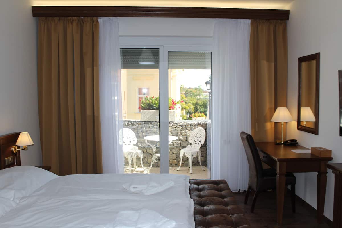 Une chambre d’hôtel comprenant un lit, un bureau, une chaise et donnant sur l’espace extérieur grâce à une porte vitrée.