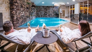 A pool area with stone walls, a hot tub, and a table with drinks.