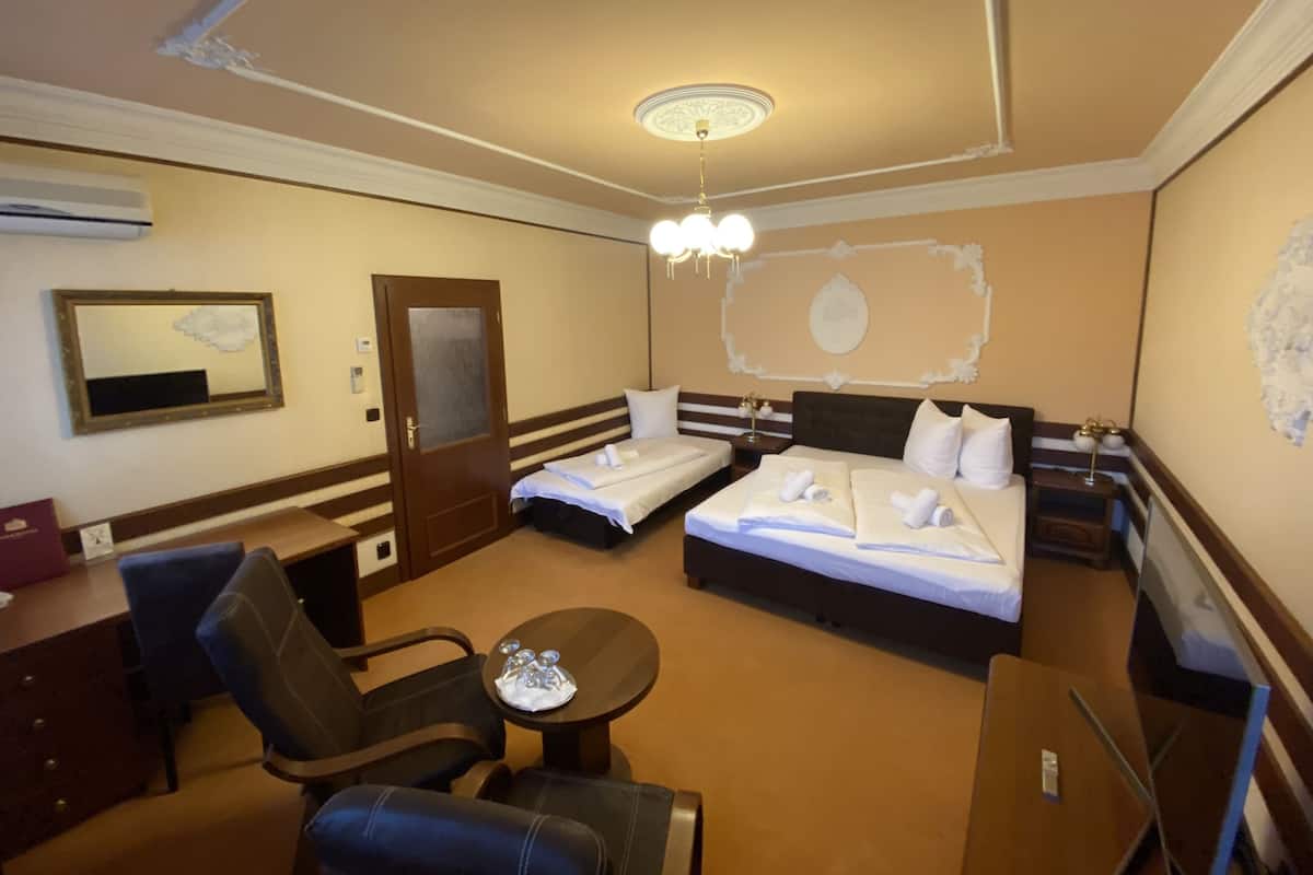 Une chambre d’hôtel avec deux lits, un bureau, une chaise, une petite table et un luminaire au plafond.
