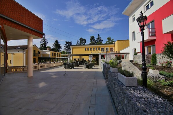 A courtyard with outdoor seating, a stone wall, and buildings with balconies. - Parkhotel Brno (Brno)