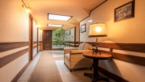 A hotel hallway with a wooden bench, a table with a lamp, and a plant.