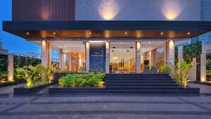 A modern hotel entrance with a glass facade, a wooden overhang, and a landscaped area with plants. - Royale Sarovar Portico Agra (Agra)