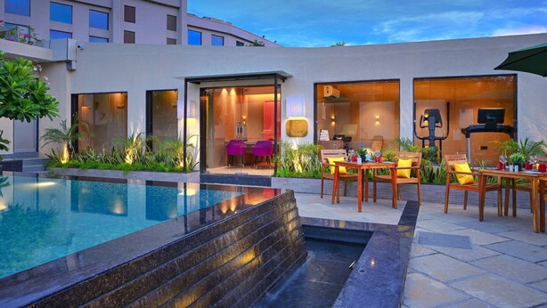 A modern hotel with an outdoor swimming pool, a patio with wooden furniture, and a well-lit interior. - Royale Sarovar Portico Agra (Agra)