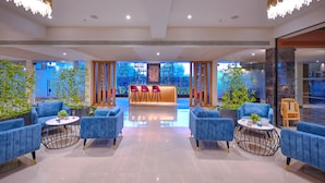A modern lobby with blue sofas, a reception desk, and potted plants. - Royale Sarovar Portico Agra (Agra)
