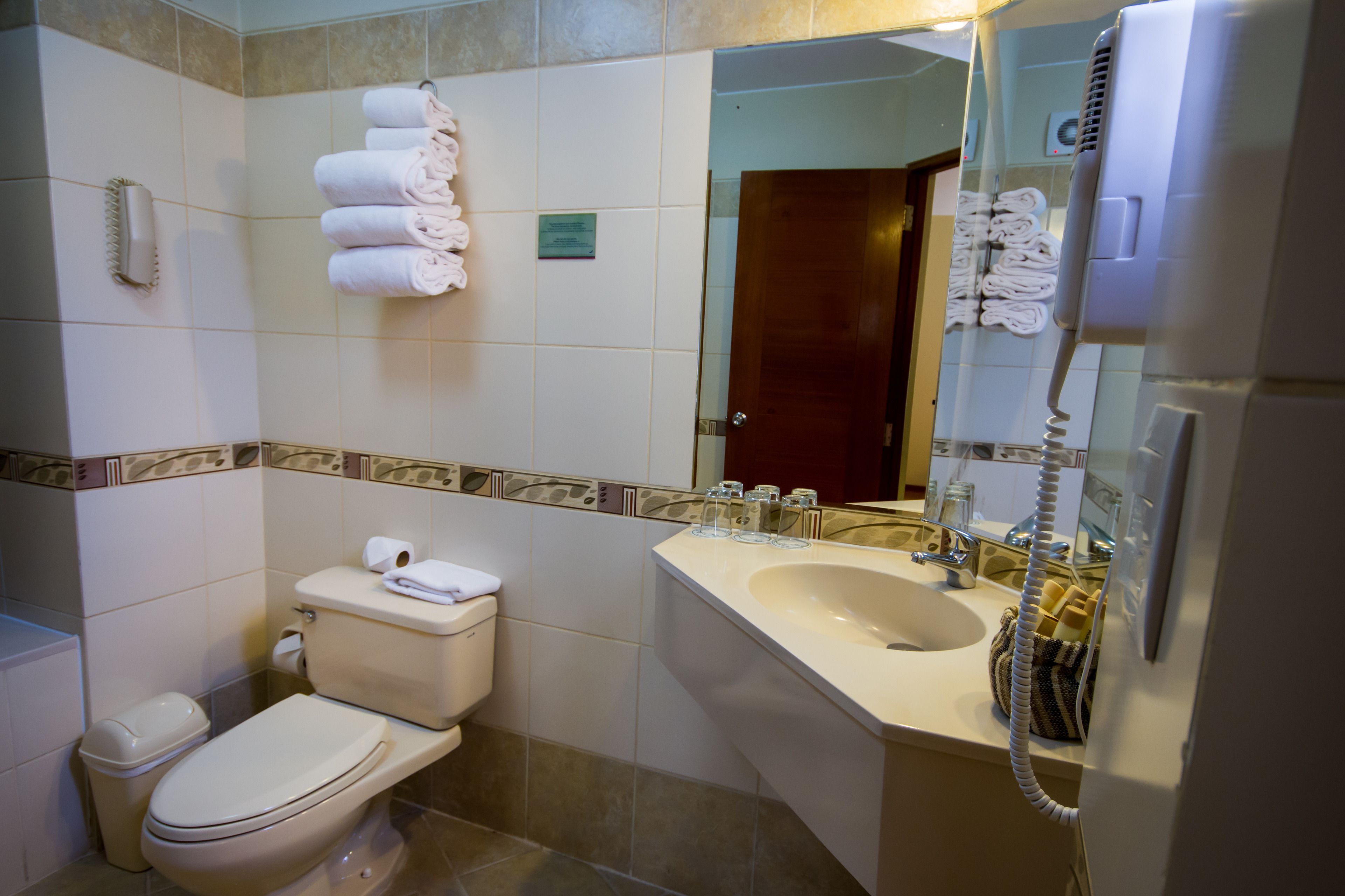 A bathroom with a toilet, sink, and a mirror. There are towels stacked on the wall and a hairdryer on the counter.