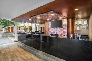 Un vestíbulo de hotel con mostrador de recepción, zona de estar y una pared decorada con diseños coloridos.